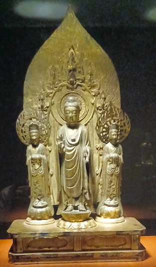 大きな舟形光背の前に中尊と両脇侍が並ぶ、飛鳥時代の金銅三尊像