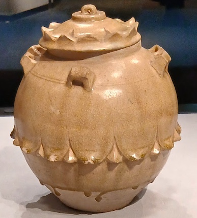 白い胎に薄い草緑色の釉がかかった青磁の壺。胴に蓮の花びらの浮彫、肩に六つの耳がつく