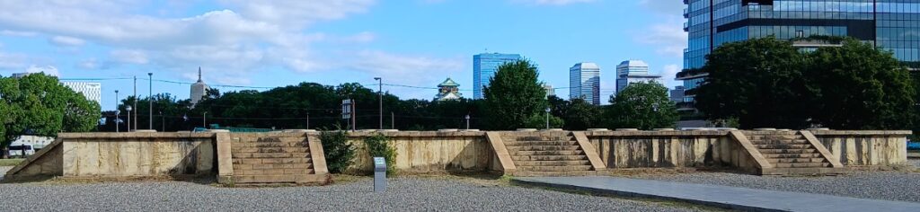 後期難波宮の大極殿の基壇。木々の向こうに大阪城の天守閣が小さく見えます
